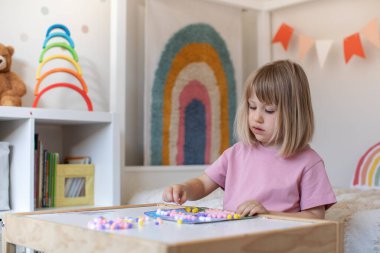 Şirin bir kız çocuk odasındaki bir masada oturuyor ve ponponlardan el işi yapıyor. Çocukların yaratıcılığı, çocuk el sanatları kavramı..