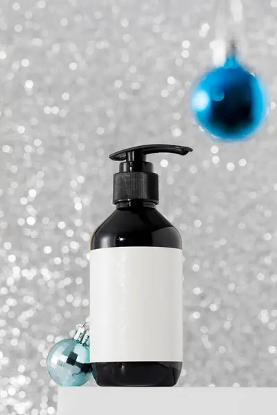 Dispenser with organic skin and hair care products on the podium with Christmas balls on a bright silver background. The concept of New Years gifts, protective skin care products in winter.