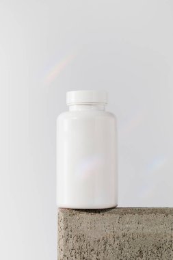 Mockup, beyaz arka planda bir kürsüde içinde haplar ya da vitaminler olan beyaz bir kavanoz. Tıbbi hazırlık kavramı..