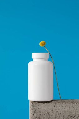 Mockup, mavi arka planda bir kürsüde içinde haplar ya da vitaminler olan beyaz bir kavanozdur. Tıbbi hazırlık kavramı..