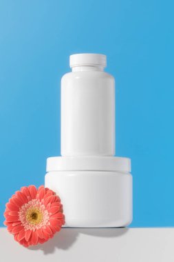 Mockup, mavi arka planda bir kürsüde içinde haplar ya da vitaminler olan beyaz bir kavanozdur. Tıbbi hazırlık kavramı, kadınlar için vitaminler