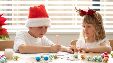 Noel kostümlü şirin erkek ve kız kardeşler odada Noel Baba 'ya bir mektup yazıyorlar. Noel hediyesi. Yeni yıl arifesi ve Noel arifesi.