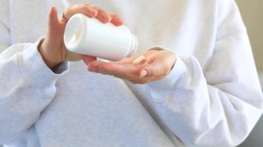 Bir kadın avucunun içine beyaz haplar ya da vitaminler döker. Yakın plan. Sağlık ve besin takviyesi kavramı.
