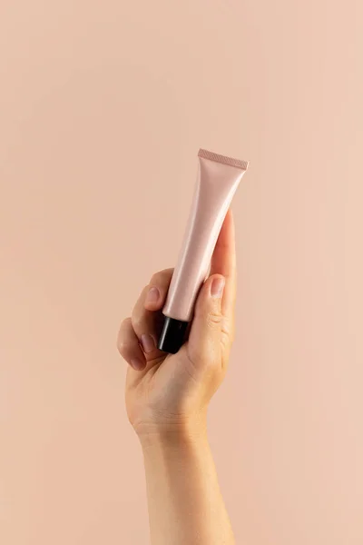 A mock-up of a pink tube with cosmetics in a womans hand on a pink background. The concept of skin care, a cosmetic product.