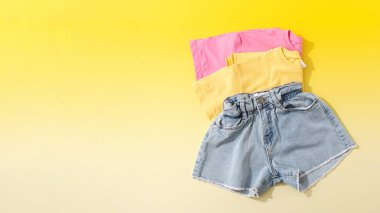 Kızlar ve kadınlar için yaz kıyafetleri. Sarı arka planda renkli tişörtlü Denim şortu. Yaz tatili için kıyafet konsepti. Boşluğu kopyala