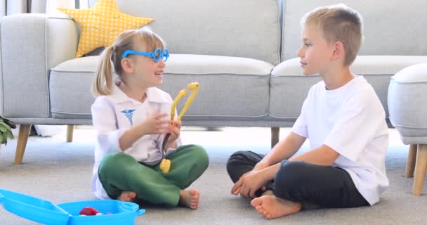 哥哥和姐姐在医院里玩耍 一个可爱的小女孩穿着医生的服装和她哥哥一起玩 保健的概念 — 图库视频影像