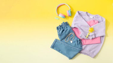 Çocuklar leylak rengi süveter ve sarı arka planda katlanmış kot pantolon. Bir kız için modaya uygun bir görünüş. Yukarıdan bak. Şık çocuk kıyafetleri. Boşluğu kopyala