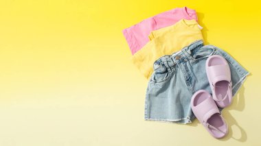 Kızlar ve kadınlar için yaz kıyafetleri. Sarı arka planda renkli tişörtlü Denim şortu. Yaz tatili için kıyafet konsepti. Boşluğu kopyala