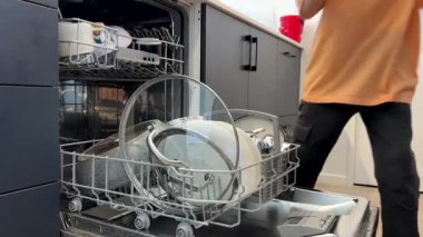 Çocuk ev işlerine yardım ediyor, bulaşık makinesinden mutfak çekmecesine temiz bulaşık koyuyor. Günlük hayatta çocuklara yardım.