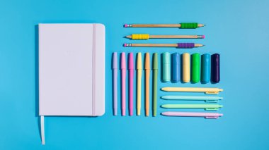 Mavi arka planda şık bir kırtasiye malzemesi. Okula dönelim. Bir defter ve renkli kalemler..