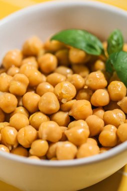 Bir tabak Ghugni, baklagiller familyasından taze fesleğen yapraklarıyla kaplanmış, sarı bir masada servis edilen bir nohut tarifi. Doğal malzemelerle yapılan lezzetli yemekler.