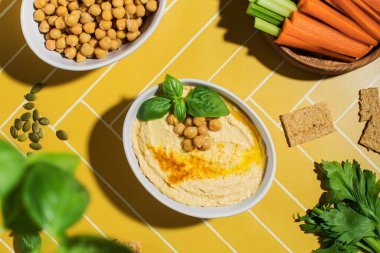 Parlak sarı arka planda taze sebzeli bir tabakta lezzetli nohut humusu. Vejetaryenlik kavramı, Doğu mutfağı..