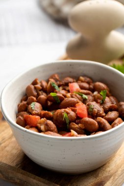 Tahta bir masada sunulan fasulye, domates ve kişnişten yapılmış lezzetli bir yemek. Bu tarif baklagillerden gelen malzemeleri taze ürünlerle birleştirir.