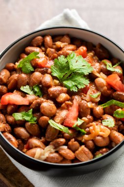 Tahta bir masada sunulan fasulye, domates ve kişnişten yapılmış lezzetli bir yemek. Bu tarif baklagillerden gelen malzemeleri taze ürünlerle birleştirir.