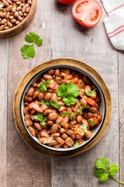 Tahta bir masada sunulan fasulye, domates ve kişnişten yapılmış lezzetli bir yemek. Bu tarif baklagillerden gelen malzemeleri taze ürünlerle birleştirir.