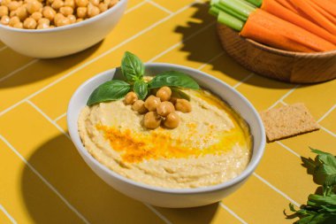 Parlak sarı arka planda taze sebzeli bir tabakta lezzetli nohut humusu. Vejetaryenlik kavramı, Doğu mutfağı..