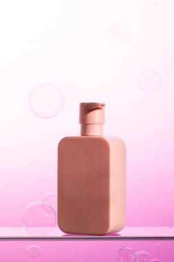 Pompalı ve kozmetik ürünleri olan pembe plastik bir şişe, mor renkli baloncuklarla çevrili cam bir rafta sergileniyor..