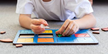 Bir çocuk halıda mantıklı bir ahşap oyun oynuyor. Montessori eğitici oyuncaklar, geometrik bulmacalar. Çocuk gelişimi için eko oyuncaklar.