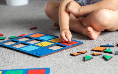 Tatlı bir kız odada yerde mantıklı bir ahşap oyun oynuyor. Çocuklar için ahşap eğitim oyuncağı. Çocuk gelişimi ve eğitim.