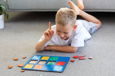 Bir çocuk halıda mantıklı bir ahşap oyun oynuyor. Montessori eğitici oyuncaklar, geometrik bulmacalar. Çocuk gelişimi için eko oyuncaklar.