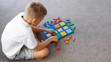 Bir çocuk halıda mantıklı bir ahşap oyun oynuyor. Montessori eğitici oyuncaklar, geometrik bulmacalar. Çocuk gelişimi için eko oyuncaklar.