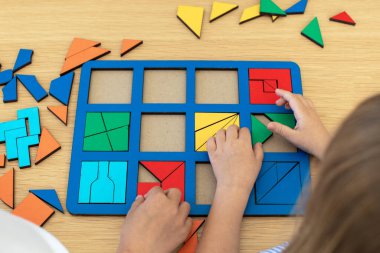 Çocuklar masada ahşap bir yapbozla oynuyorlar. Montessori yöntemini kullanan çocuklar için eğitici mantık oyuncakları.