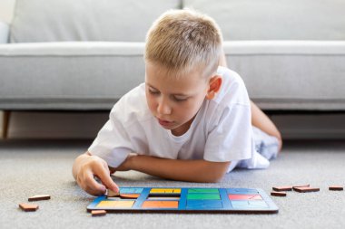 Bir çocuk halıda mantıklı bir ahşap oyun oynuyor. Montessori eğitici oyuncaklar, geometrik bulmacalar. Çocuk gelişimi için eko oyuncaklar.