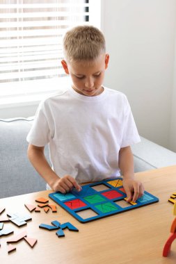 Şirin bir çocuk, odada bir masada mantıklı bir ahşap oyun oynuyor. Çocuklar için ahşap eğitim oyuncağı. Bir çocuğun gelişimi ve yetiştirilmesi.
