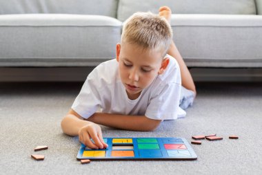 Bir çocuk halıda mantıklı bir ahşap oyun oynuyor. Montessori eğitici oyuncaklar, geometrik bulmacalar. Çocuk gelişimi için eko oyuncaklar.