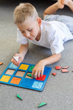Bir çocuk halıda mantıklı bir ahşap oyun oynuyor. Montessori eğitici oyuncaklar, geometrik bulmacalar. Çocuk gelişimi için eko oyuncaklar.