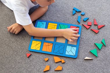 Bir çocuk halıda mantıklı bir ahşap oyun oynuyor. Montessori eğitici oyuncaklar, geometrik bulmacalar. Çocuk gelişimi için eko oyuncaklar.