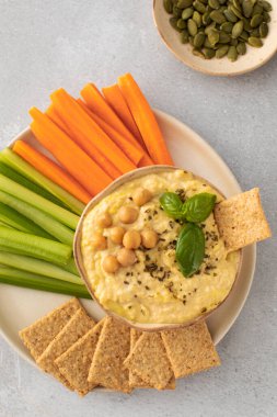 Havuç ve kereviz çubuklarıyla servis edilen bir humus tabağı. Masanın üzerinde mükemmel bir doğal yiyecek ve sebze kombinasyonu.