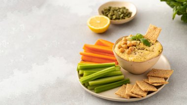 Havuç ve kereviz çubuklarıyla servis edilen bir humus tabağı. Masada doğal yiyecek ve sebzelerin mükemmel bir kombinasyonu. Uzayı kopyala Pankart