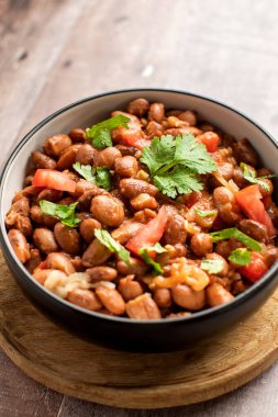 Tahta bir masada sunulan fasulye, domates ve kişnişten yapılmış lezzetli bir yemek. Bu tarif baklagillerden gelen malzemeleri taze ürünlerle birleştirir.