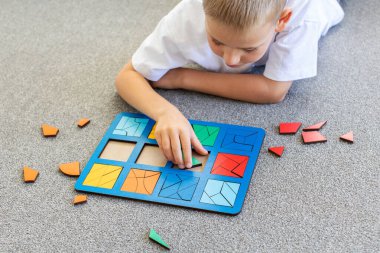 Bir çocuk halıda mantıklı bir ahşap oyun oynuyor. Montessori eğitici oyuncaklar, geometrik bulmacalar. Çocuk gelişimi için eko oyuncaklar.
