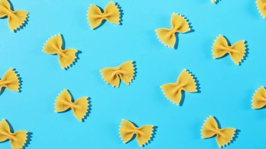 Pişmemiş papyonlu makarna, mavi arka plana serpilmiş farfalle dekoratif desenli, dokuyu ve şekli vurguluyor.