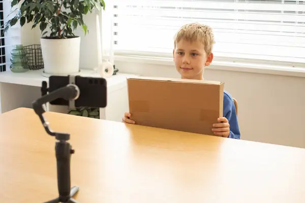 Smiling boy filming an unboxing video blog about a toy, using a microphone and camera. The concept of video blogging and unpacking.