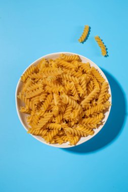 Pişmemiş fusilli makarna mavi arka planda beyaz bir kasede döner. Yemek ve yemek kavramları için mükemmeldir.