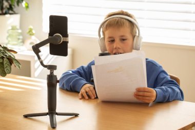 Çocuk kulaklıklar ve mikrofonla bir podcast kaydediyor. Etkilenen bir blogcu çocuk içeriği kaydeder. Bloglama ve podcast kavramı.