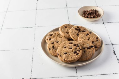 Yanında ekstra çikolata parçacıklı kurabiyeler, beyaz fayanslı arka planda..