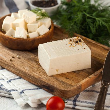 Köy ahşap kesim tahtasındaki taze peynir otlar ve baharatlarla süslenmiş, yanında domates ile servis edilen geleneksel bir Akdeniz atıştırmalığı..