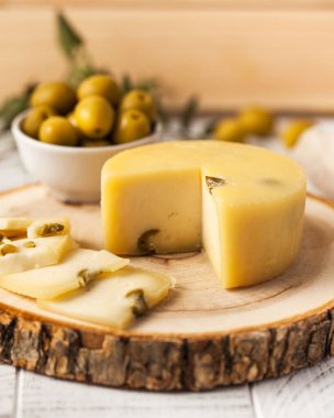 Artisan Caciotta cheese with olives, displayed on a rustic wooden board, complemented by a bowl of green olives in the background clipart