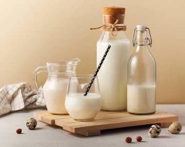 Ahşap bir tahtanın üzerinde bıldırcın yumurtası ve fındıklı çeşitli süt kapları, sağlıklı ve sade bir mutfak düzeneği sergiliyor. Süt ürünü