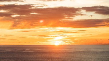 Bali 'de okyanusun üzerinde çarpıcı bir günbatımı, canlı turuncu ve kırmızı renkler gökyüzünü boyuyor, huzurlu ve resimsel bir manzara yaratıyor..