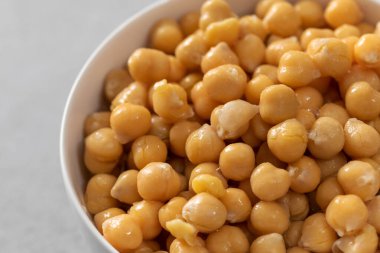 Açık gri arka planda küçük kasede konserve nohutlar. İşlenmiş garbanzo fasulyeleri beton masada yenmeye hazır. Protein besin içerir