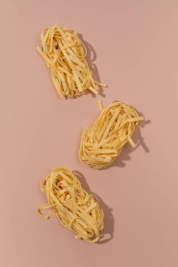 Pişmemiş tagliatelle makarna yuvaları pembe bir zemin üzerine dizilmiş, yaratıcı ve minimalist İtalyan mutfağı sergileniyor.