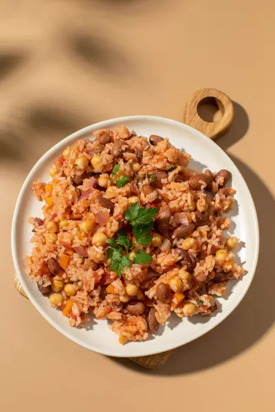 stock image Jambalaya with rice, chickpeas and kidney beans on beige table upper view. Nutritious vegan dish and leaves shadows