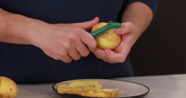 Bir adam çiğ patatesleri bıçakla soyar. Yemek pişirme süreci. Video Talimatları