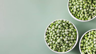 Donmuş yeşil bezelyelerle dolu üç beyaz kase yeşil arka planda sıralanmış. Boşluğu kopyala