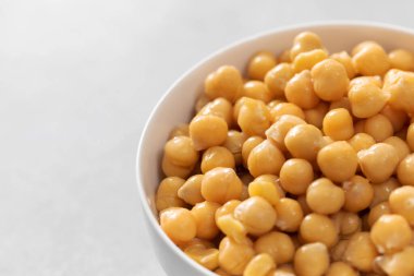 Açık gri arka planda küçük kasede konserve nohutlar. İşlenmiş garbanzo fasulyeleri beton masada yenmeye hazır. Protein besin içerir